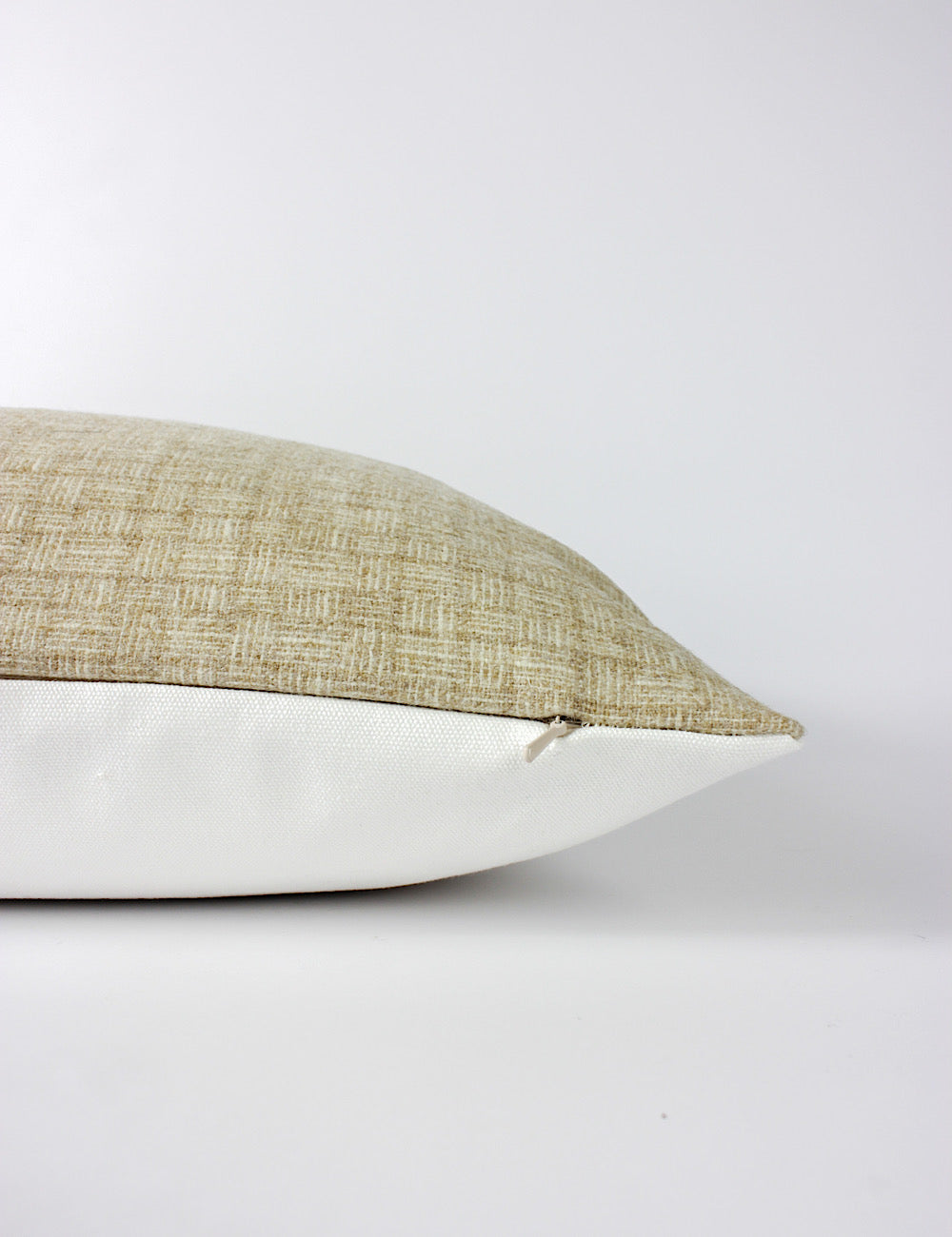 Side view of a neutral toned scatter cushion with a subtle small scale woven pattern across the front and a plain white back. Hidden zip.