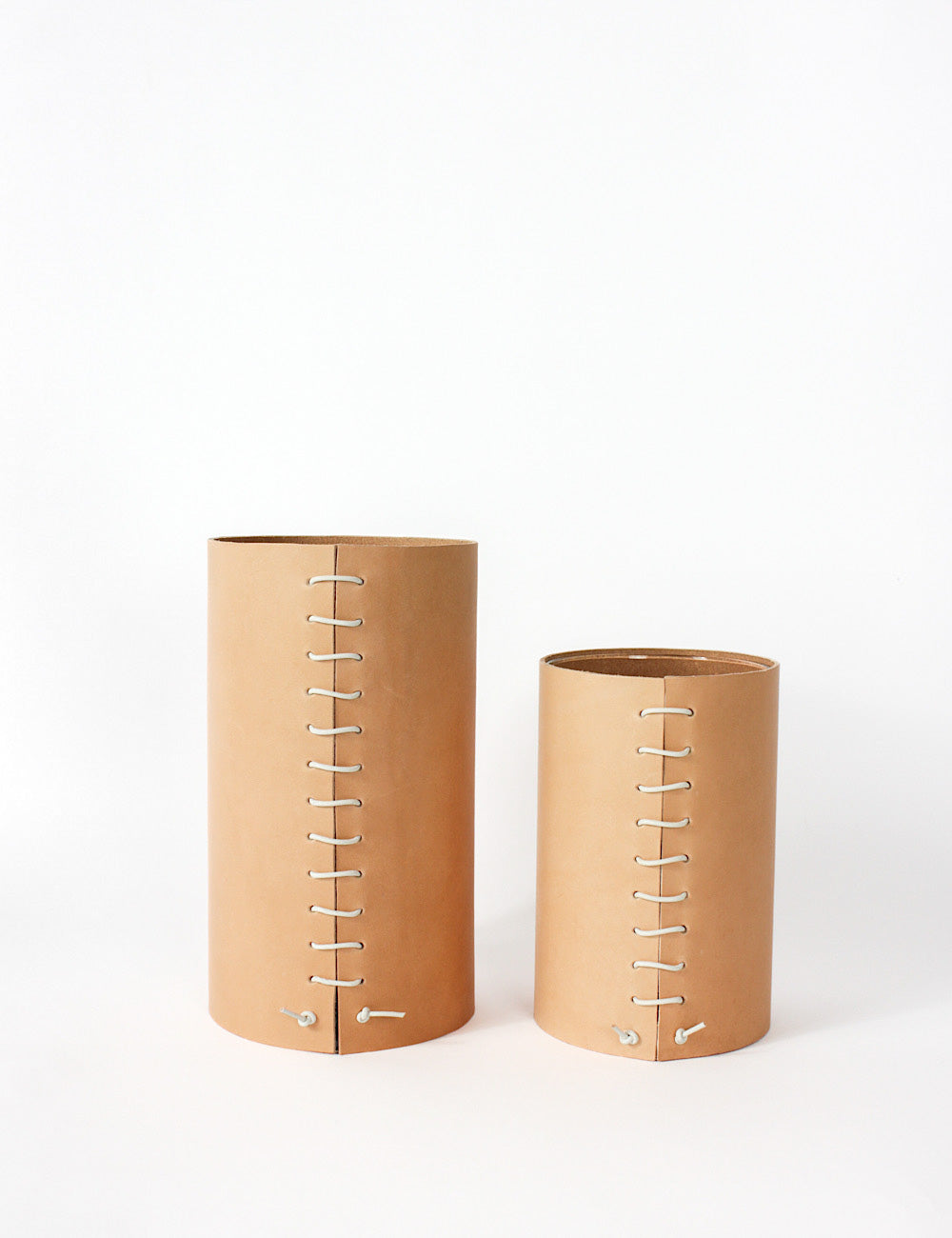Two Leather Wrapped vases, one small, one medium. Cylindrical in shape, with a leather stitched detailing going down the middle where both leather ends meet. 