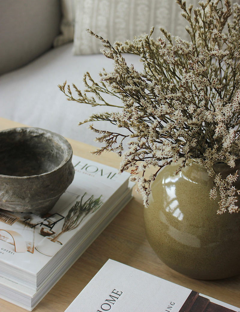 Styled image capturing a dark green ceramic vase on a coffee table. 