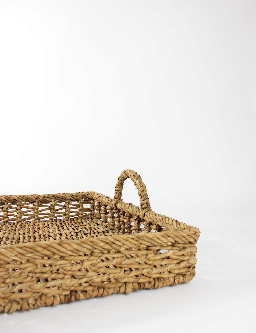 Close up side shot of a rattan tray with handles on two opposite ends.
