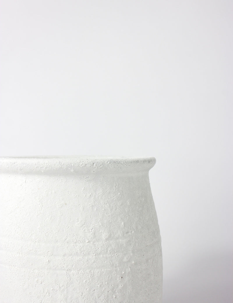 Close up of a white terracotta pot with a textured finish and bottle neck top opening. 